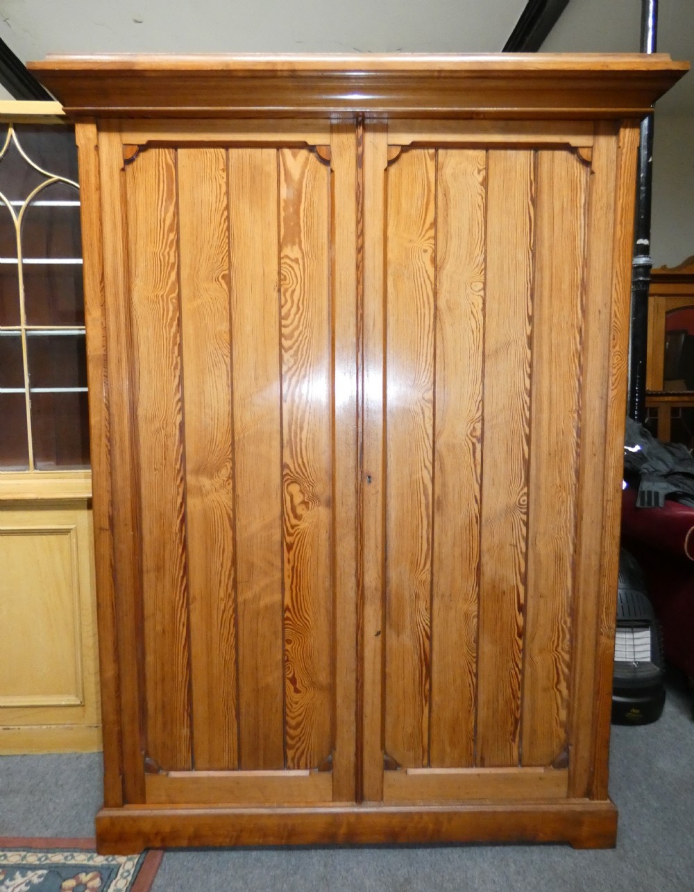 A tall Victorian pine housekeepers cupboard featuring two vertical plank-panelled doors, a projected moulded top cornice, and a sturdy plinth base. View VII