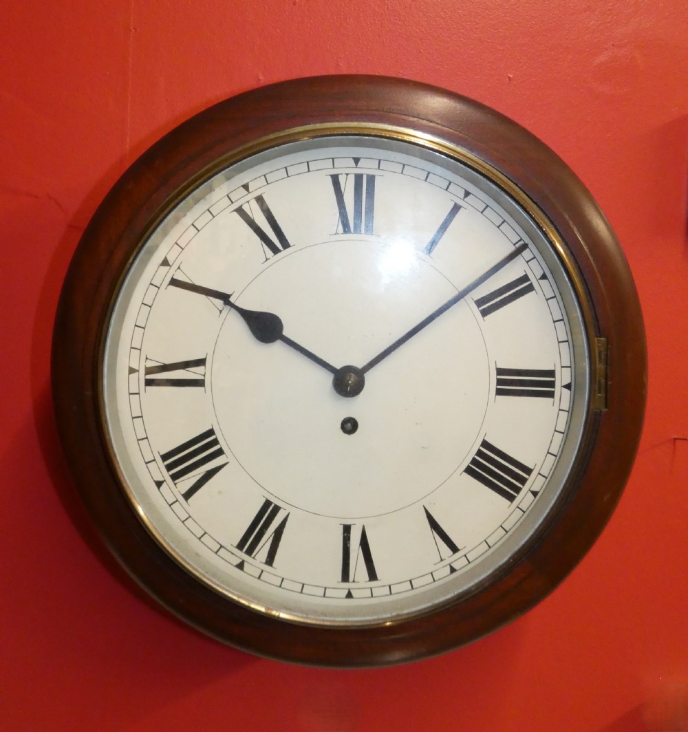 An antique circular wall clock featuring a turned mahogany surround, white painted dial with black Roman numerals, and a brass glass bezel.
