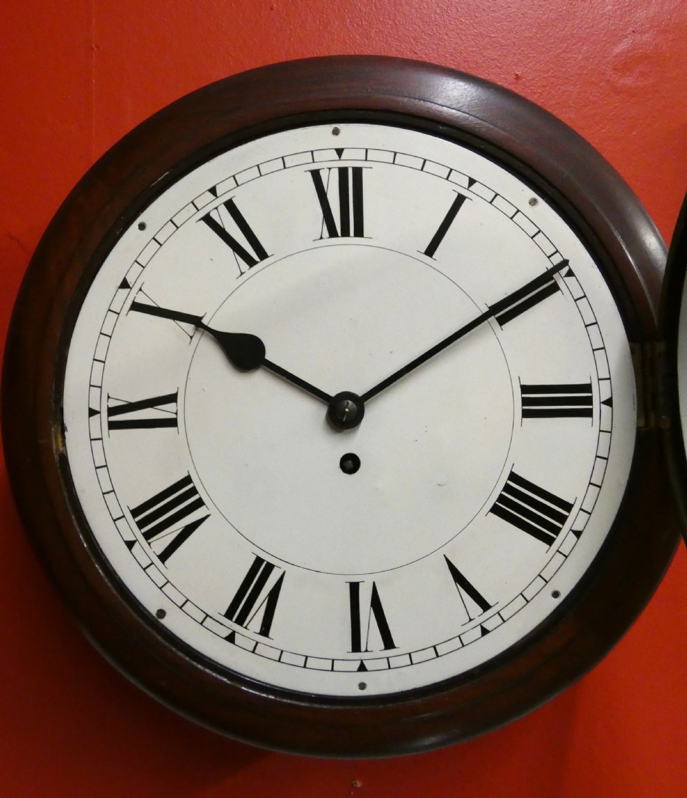 An antique circular wall clock featuring a turned mahogany surround, white painted dial with black Roman numerals, and a brass glass bezel. View II