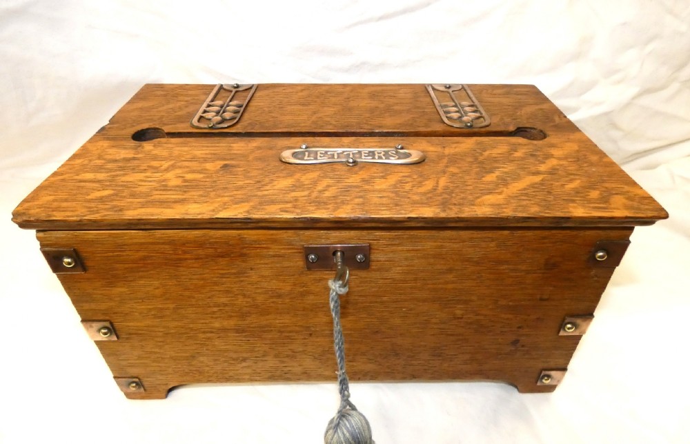 An antique Arts and Crafts solid oak letter box featuring decorative copper strap hinges, corner brackets, a top letter slot, and a central embossed copper plaque reading LETTERS.