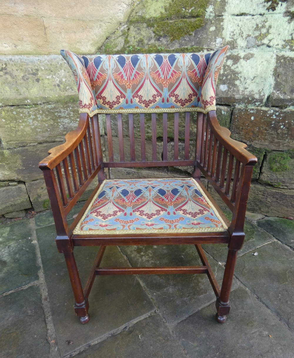 An Arts and Crafts wooden armchair featuring a slatted backrest, shaped armrests, turned front legs, and colourful patterned fabric upholstery.