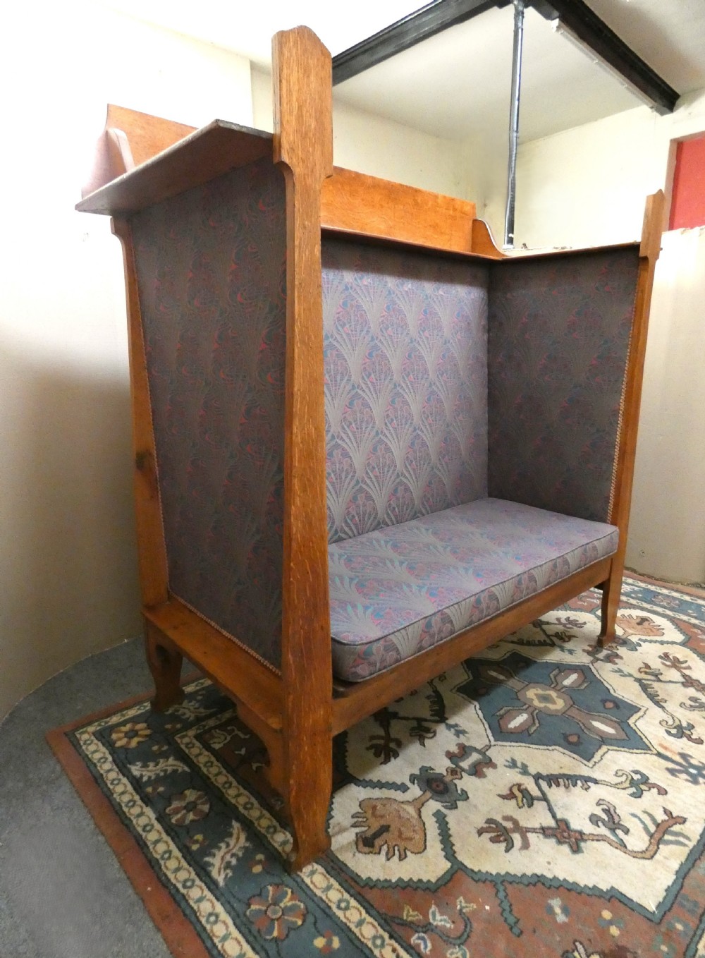 An Arts and Crafts period solid oak high-back settle featuring upholstered side panels and a cushioned seat.
