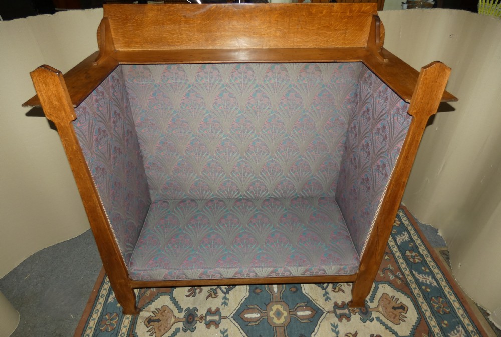 An Arts and Crafts period solid oak high-back settle featuring upholstered side panels and a cushioned seat. View V