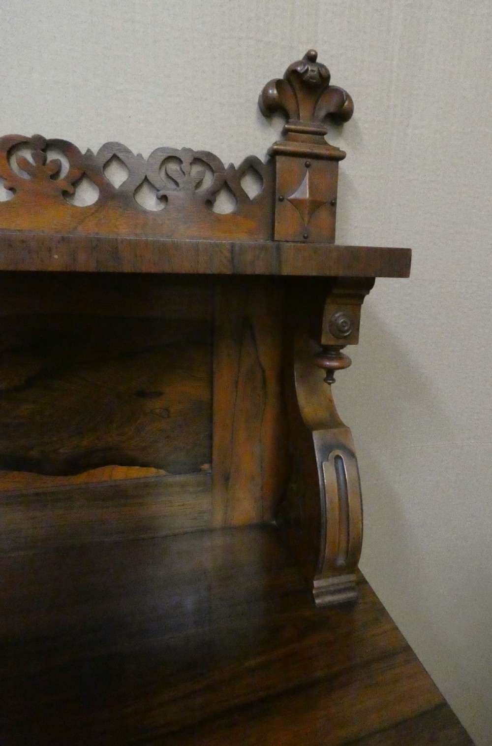 A Victorian rosewood breakfront chiffonier featuring a upper gallery shelf, central panelled cupboard doors, and outer doors with intricate pierced fretwork over light blue fabric backing. View V