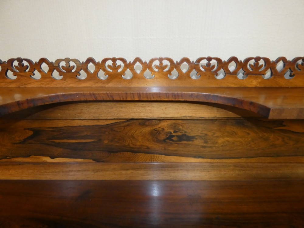 A Victorian rosewood breakfront chiffonier featuring a upper gallery shelf, central panelled cupboard doors, and outer doors with intricate pierced fretwork over light blue fabric backing. View VI