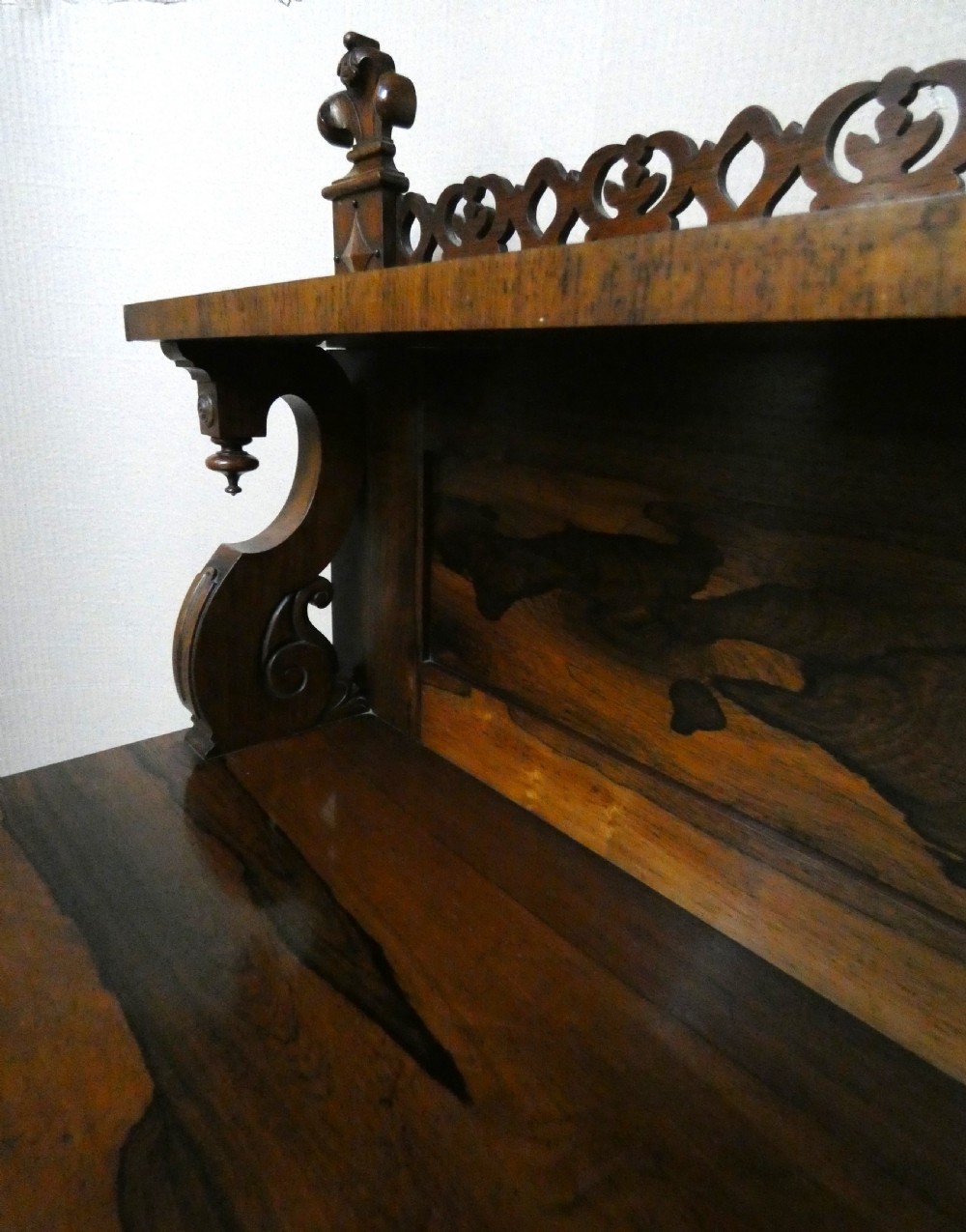 A Victorian rosewood breakfront chiffonier featuring a upper gallery shelf, central panelled cupboard doors, and outer doors with intricate pierced fretwork over light blue fabric backing. View VII