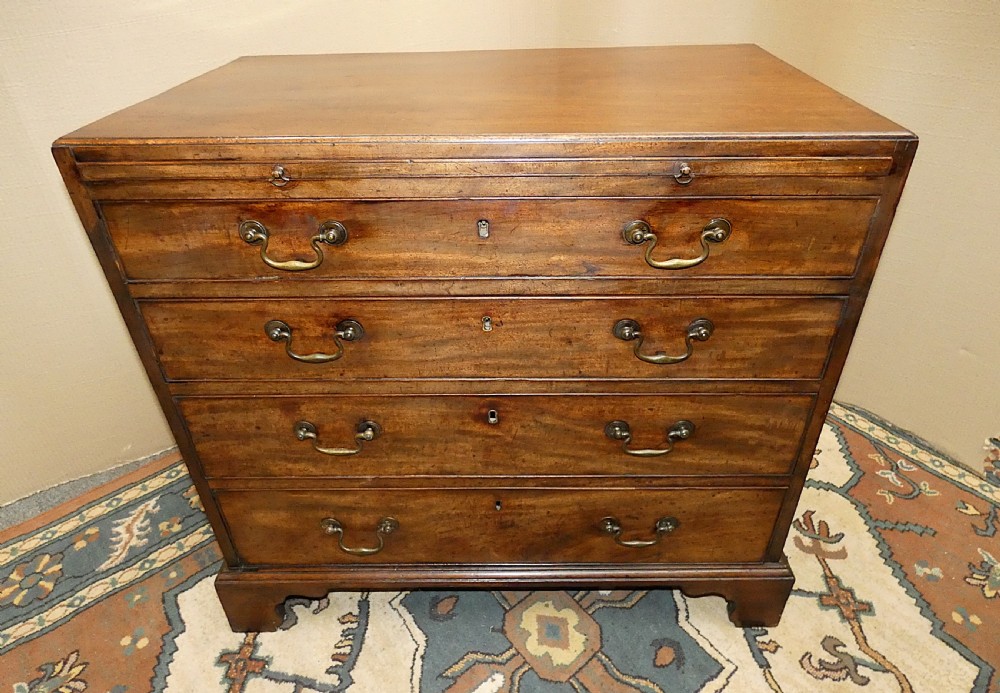 A small Georgian mahogany bachelors chest featuring four graduated drawers with brass swan-neck handles, keyholes, and bracket feet.