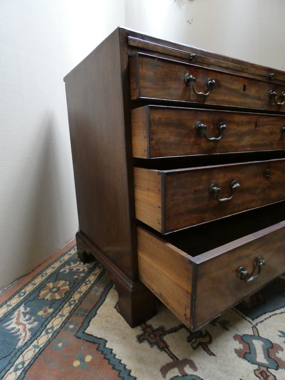A small Georgian mahogany bachelors chest featuring four graduated drawers with brass swan-neck handles, keyholes, and bracket feet. View IV