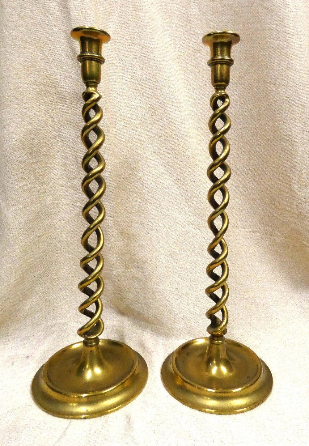 A pair of tall brass candlesticks featuring open barley twist stems and circular moulded bases.
