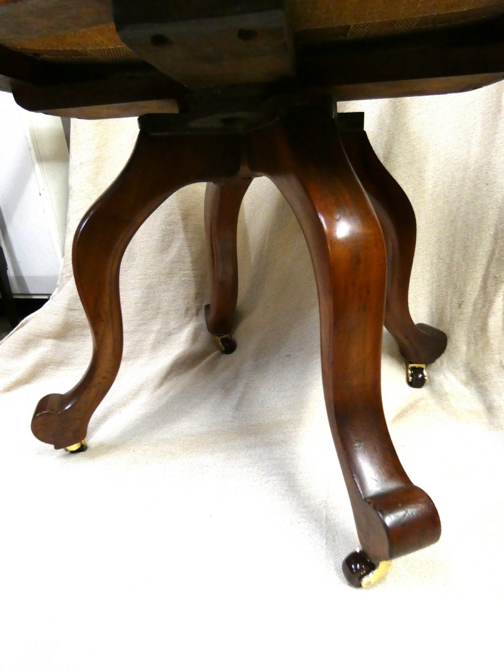 An antique revolving wood desk chair featuring a carved sunburst crest rail, curved armrests, a brown leather seat with brass stud trimming, and splayed legs on castors. View V