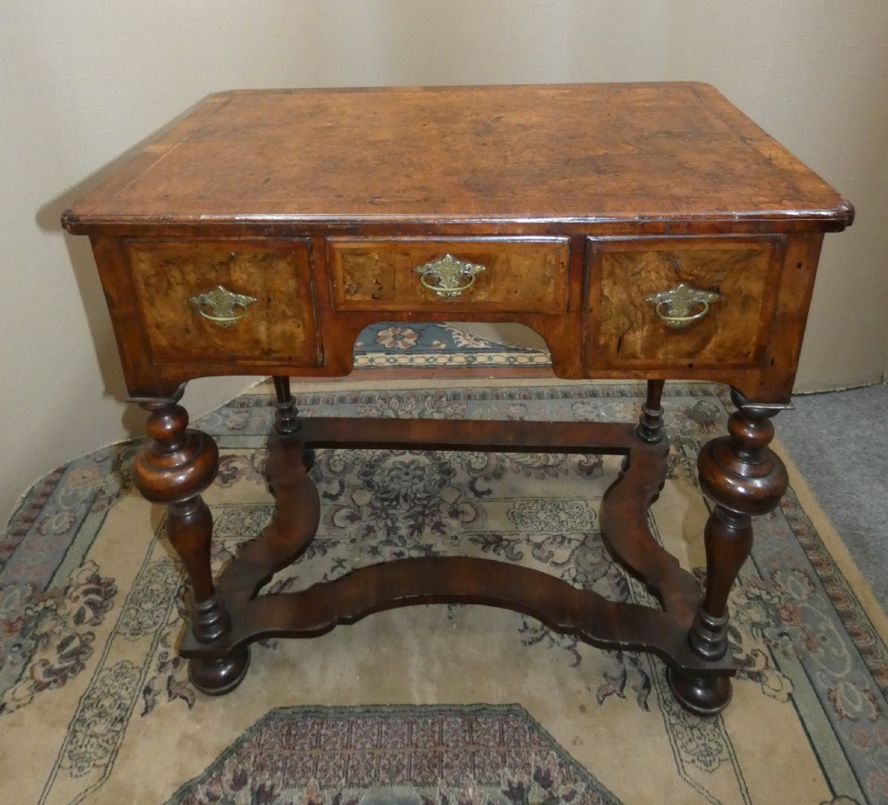 An 18th-century walnut lowboy table featuring three drawers with brass handles, turned legs, and a wavy shaped stretcher base.