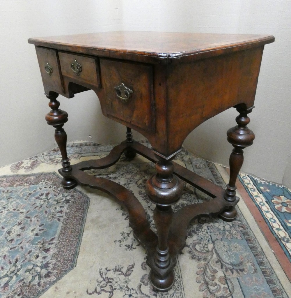An 18th-century walnut lowboy table featuring three drawers with brass handles, turned legs, and a wavy shaped stretcher base. View V