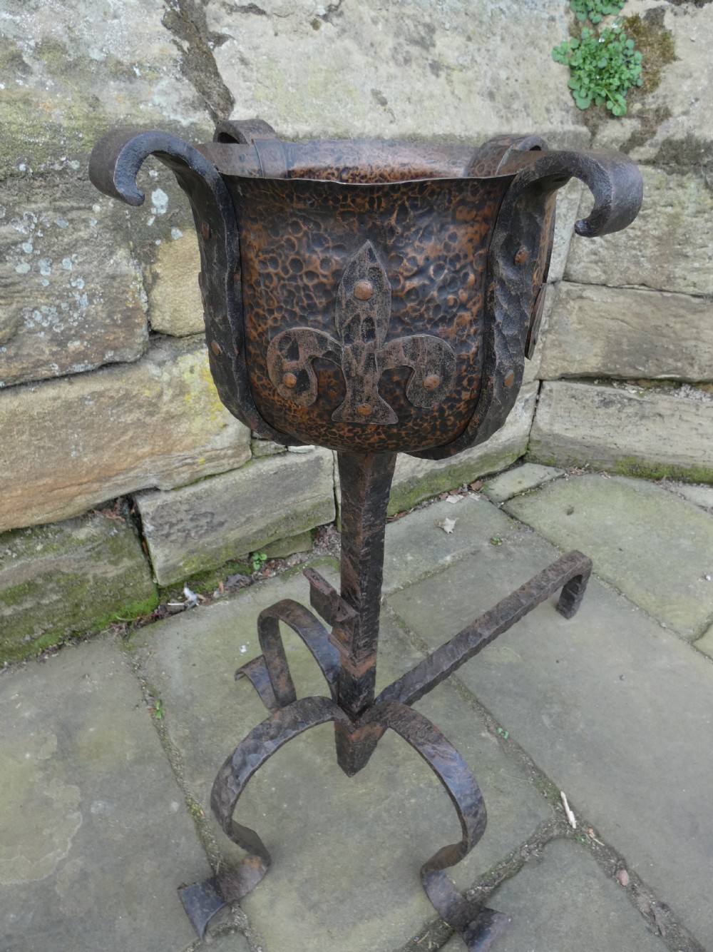 A pair of wrought iron andirons featuring scrolled legs, upright stems, and hammered copper basin tops decorated with fleur-de-lis motifs. View III