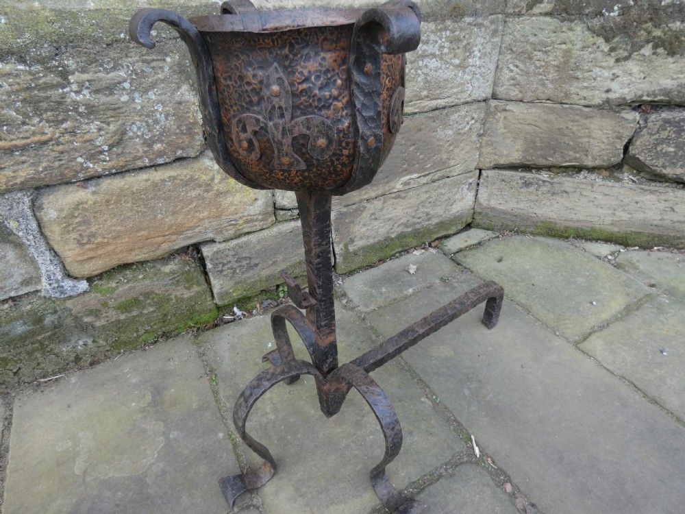 A pair of wrought iron andirons featuring scrolled legs, upright stems, and hammered copper basin tops decorated with fleur-de-lis motifs. View V