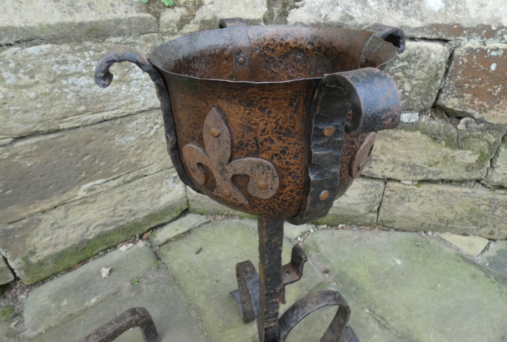 A pair of wrought iron andirons featuring scrolled legs, upright stems, and hammered copper basin tops decorated with fleur-de-lis motifs. View VI