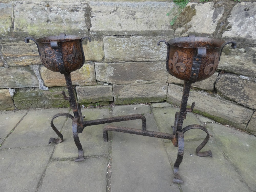 A pair of wrought iron andirons featuring scrolled legs, upright stems, and hammered copper basin tops decorated with fleur-de-lis motifs. View VIII