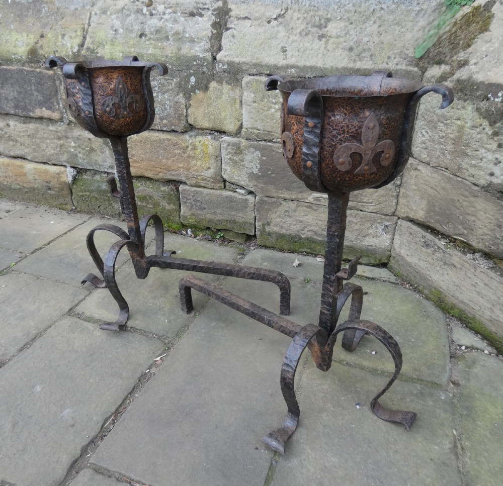 A pair of wrought iron andirons featuring scrolled legs, upright stems, and hammered copper basin tops decorated with fleur-de-lis motifs. View IX