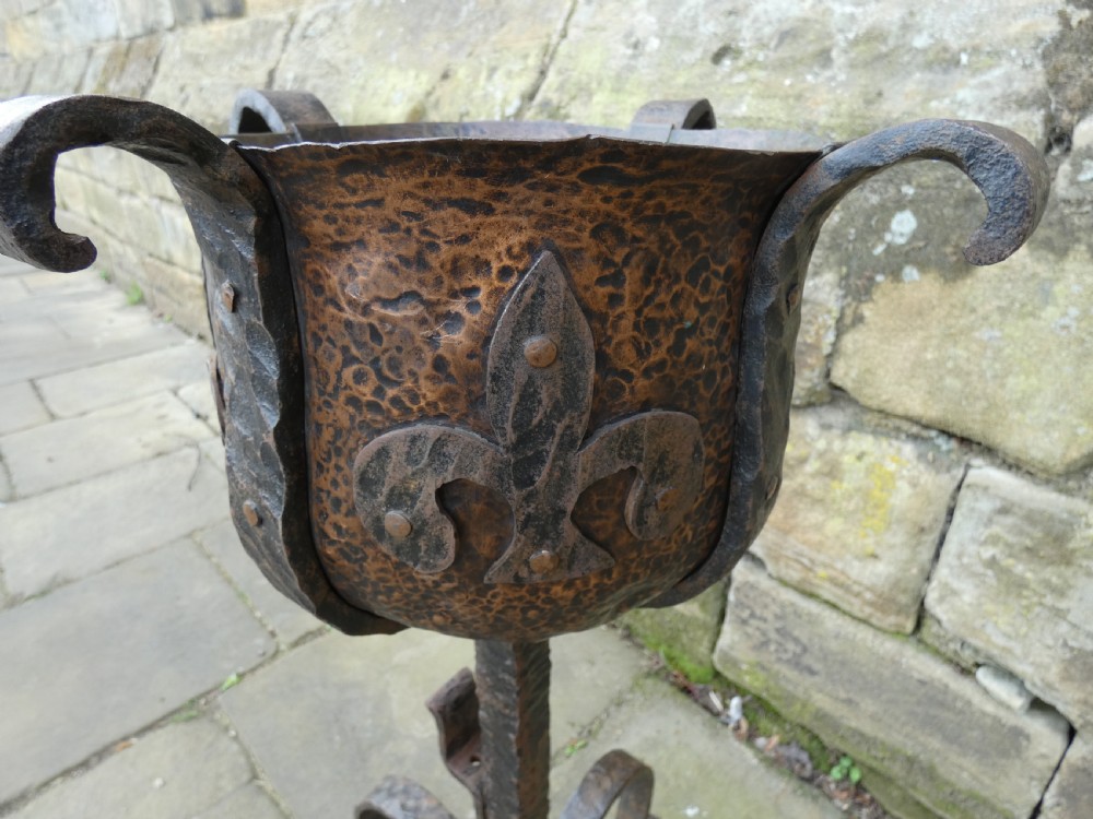 A pair of wrought iron andirons featuring scrolled legs, upright stems, and hammered copper basin tops decorated with fleur-de-lis motifs. View XI