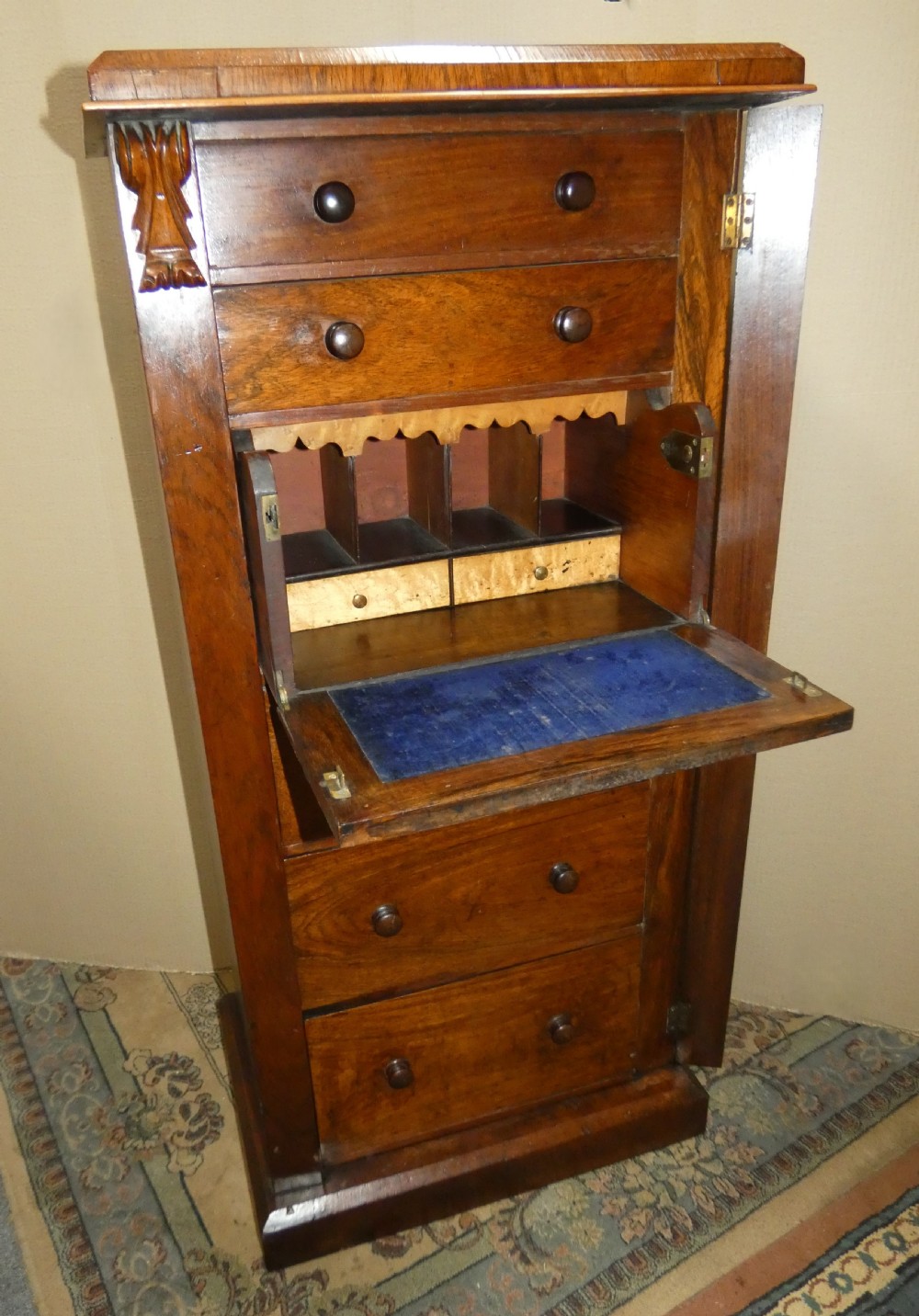 A tall Victorian rosewood Wellington chest featuring turned wooden knobs, carved upper corbels, and an open drop-front secretaire drawer revealing internal pigeonholes and small drawers.