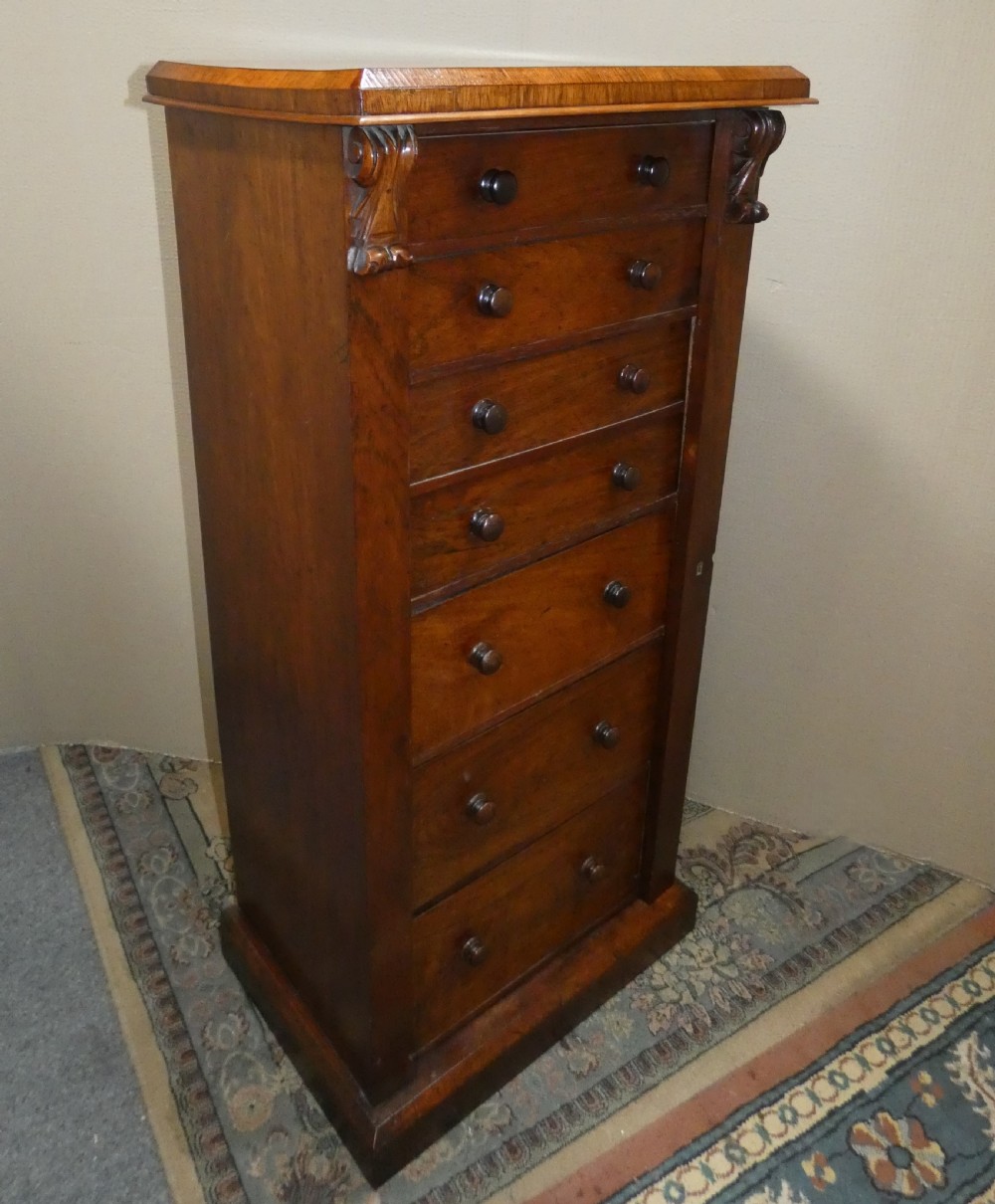 A tall Victorian rosewood Wellington chest featuring turned wooden knobs, carved upper corbels, and an open drop-front secretaire drawer revealing internal pigeonholes and small drawers. View II