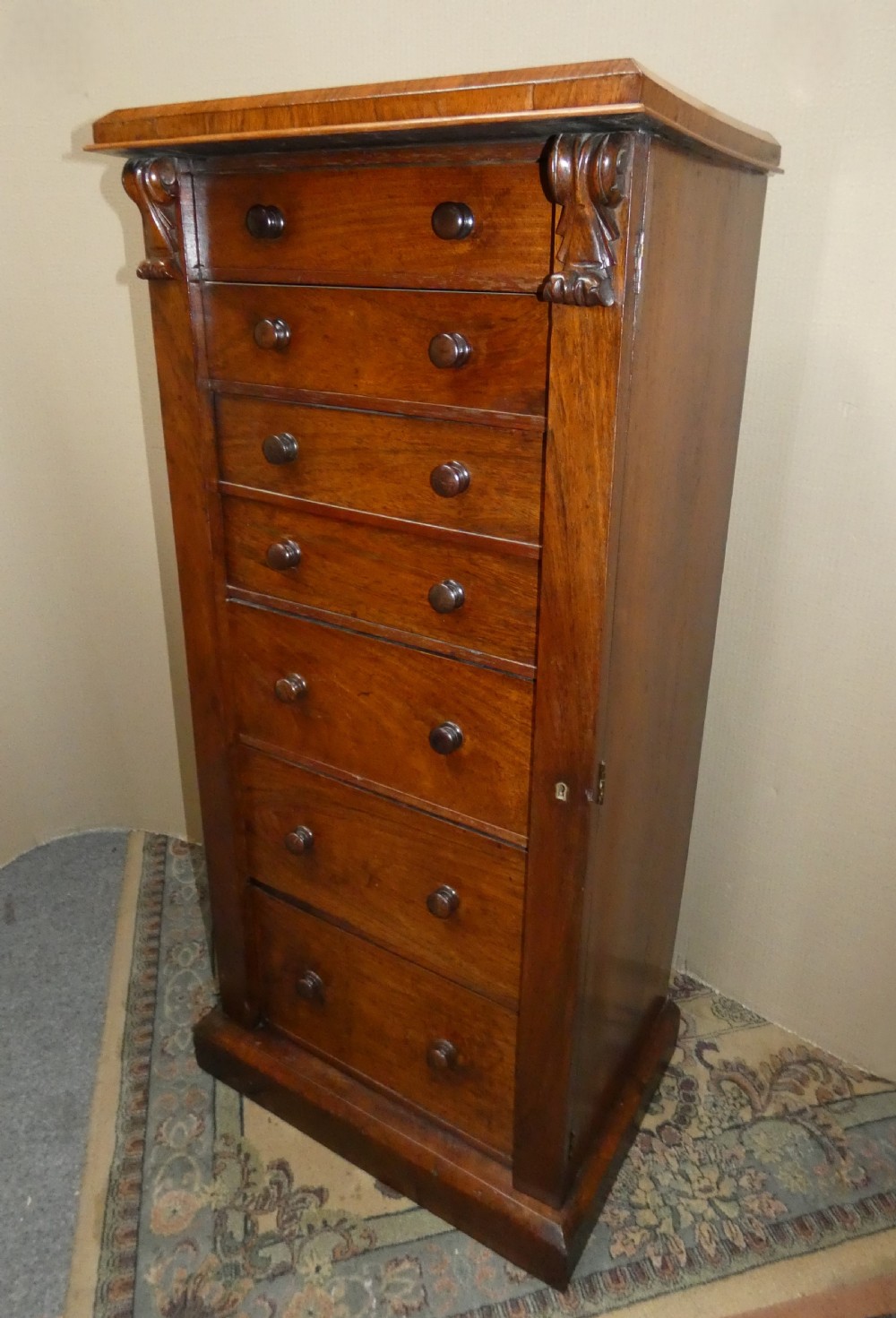 A tall Victorian rosewood Wellington chest featuring turned wooden knobs, carved upper corbels, and an open drop-front secretaire drawer revealing internal pigeonholes and small drawers. View III