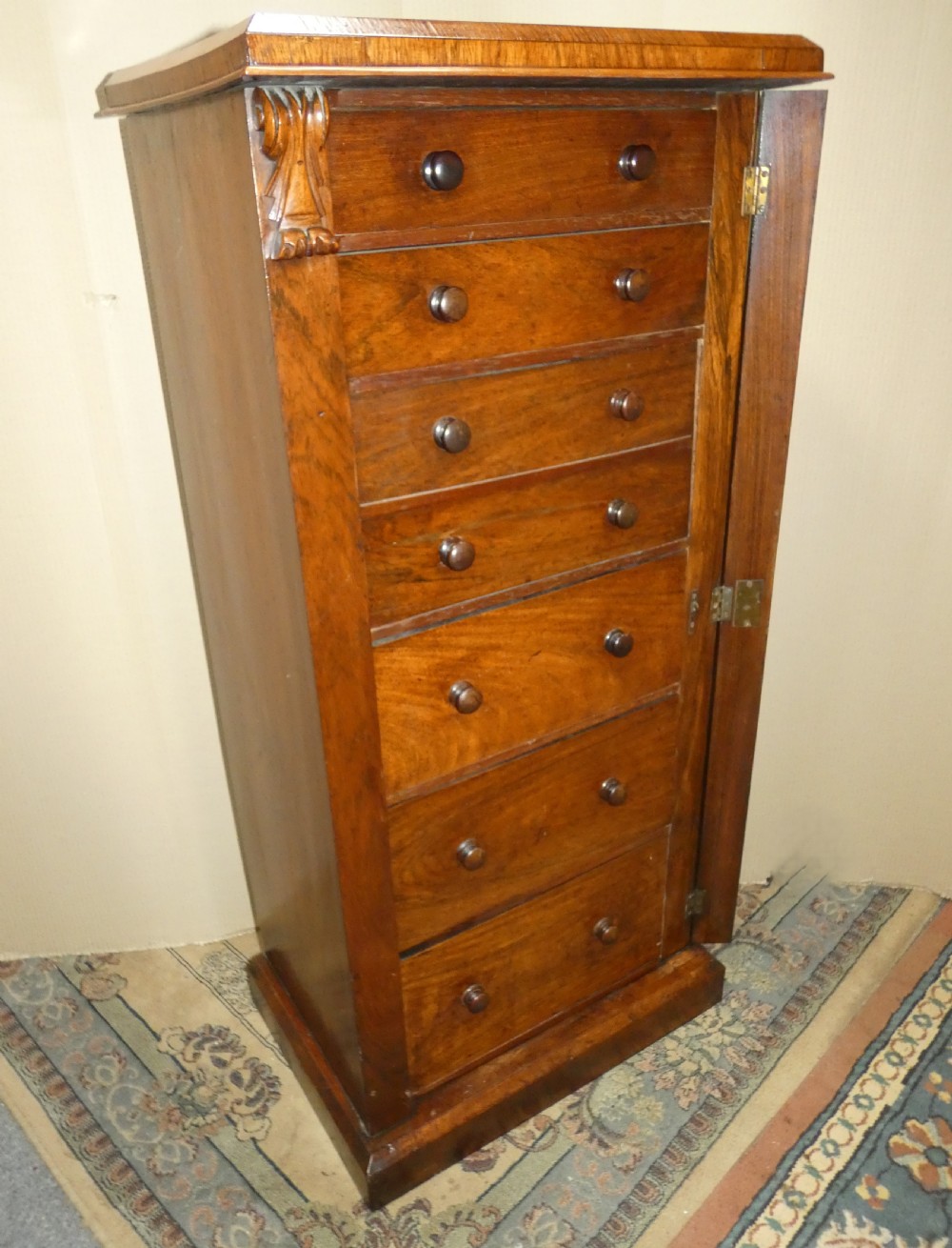 A tall Victorian rosewood Wellington chest featuring turned wooden knobs, carved upper corbels, and an open drop-front secretaire drawer revealing internal pigeonholes and small drawers. View V