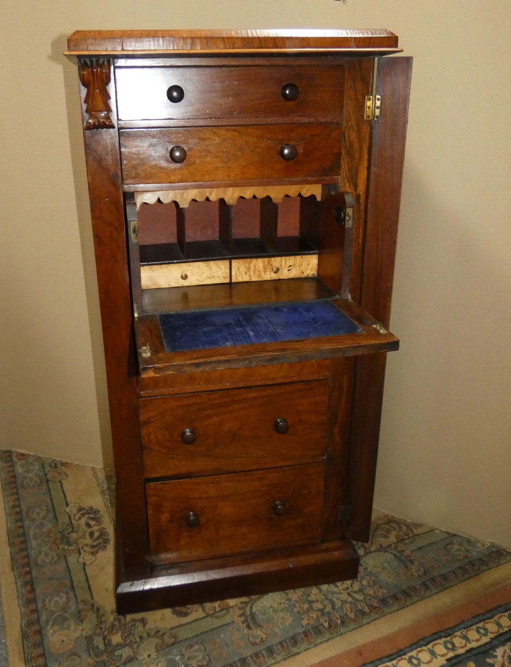 A tall Victorian rosewood Wellington chest featuring turned wooden knobs, carved upper corbels, and an open drop-front secretaire drawer revealing internal pigeonholes and small drawers. View VI