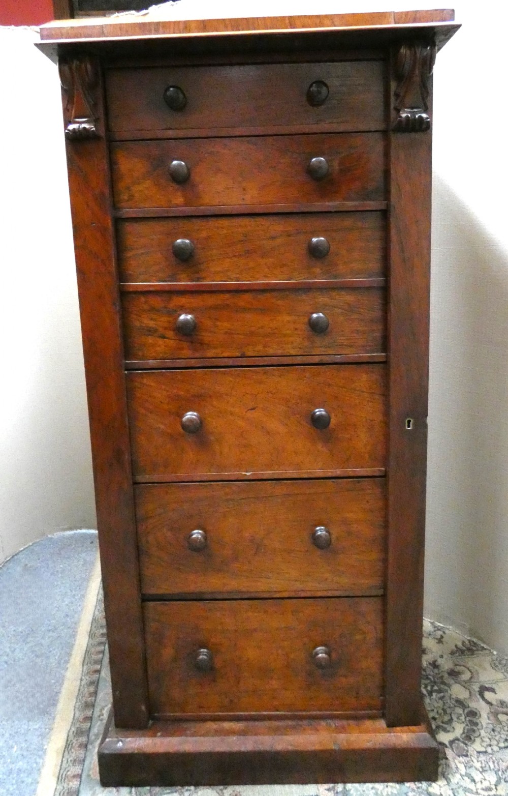 A tall Victorian rosewood Wellington chest featuring turned wooden knobs, carved upper corbels, and an open drop-front secretaire drawer revealing internal pigeonholes and small drawers. View VII
