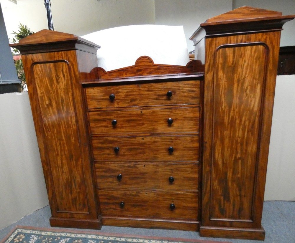 An antique Victorian mahogany combination wardrobe featuring a central stack of five drawers flanked by two tall flanking side cupboards with pediment tops.