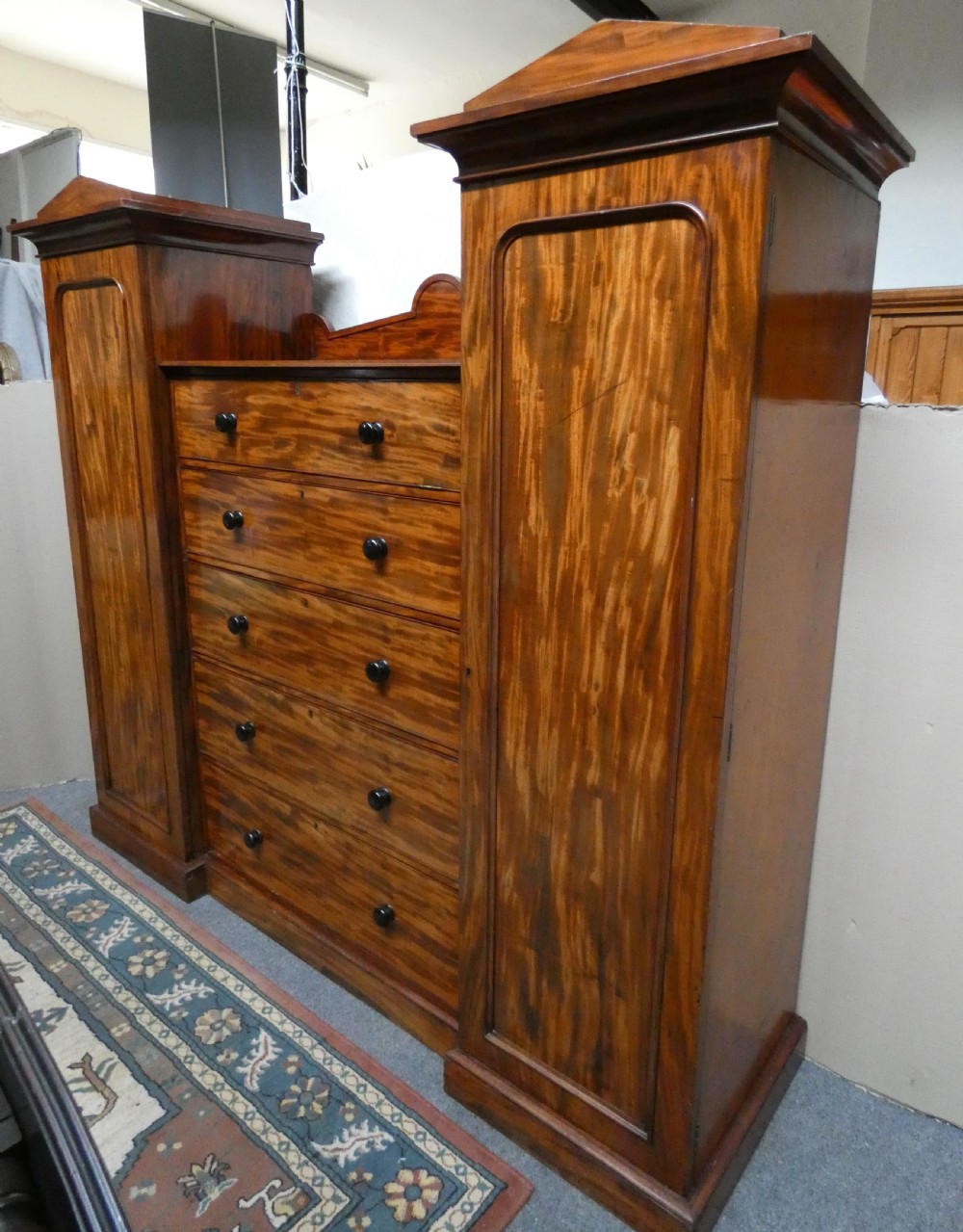 An antique Victorian mahogany combination wardrobe featuring a central stack of five drawers flanked by two tall flanking side cupboards with pediment tops. View V