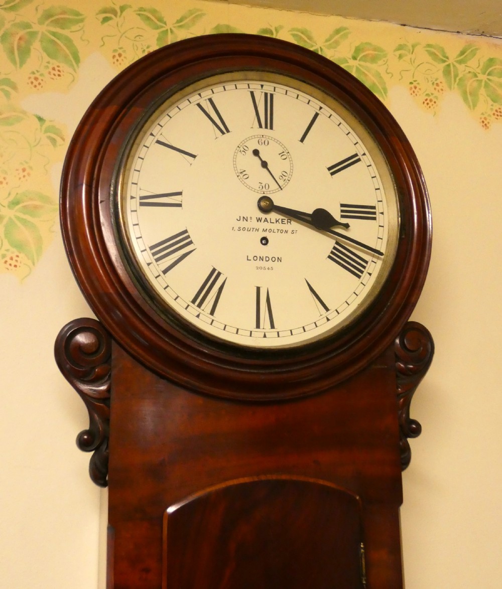 A Victorian flame mahogany regulator wall clock featuring a round white dial with Roman numerals above a drop trunk case with carved scrolls. View II