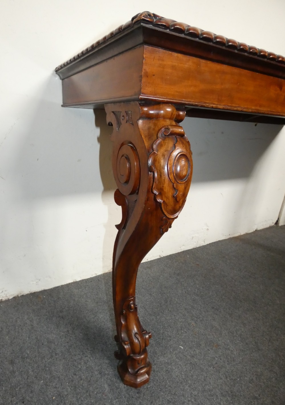 A William IV mahogany console table featuring a light marble top, gadrooned apron rim, and carved scroll front legs. View IV