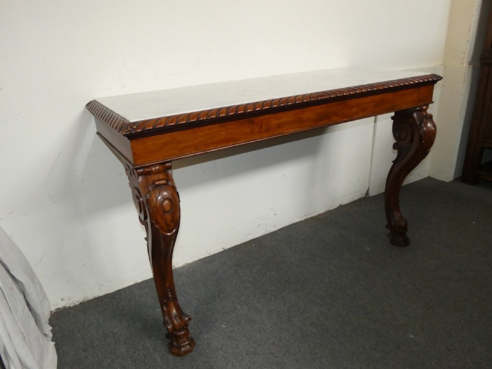 A William IV mahogany console table featuring a light marble top, gadrooned apron rim, and carved scroll front legs. View V