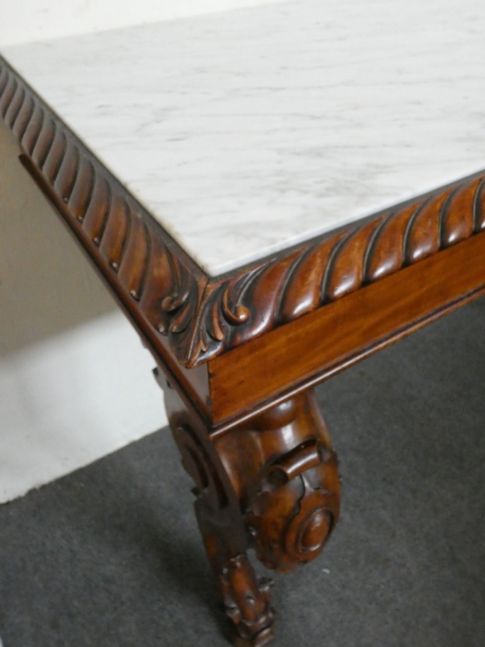 A William IV mahogany console table featuring a light marble top, gadrooned apron rim, and carved scroll front legs. View VI