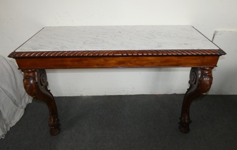 A William IV mahogany console table featuring a light marble top, gadrooned apron rim, and carved scroll front legs. View VII