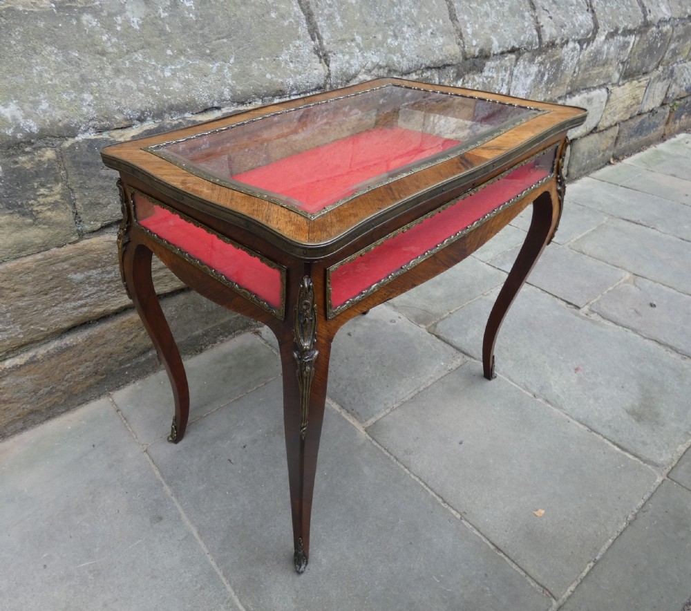 A French style rosewood bijouterie table featuring glass panels, red velvet interior lining, brass mounts, and cabriole legs.