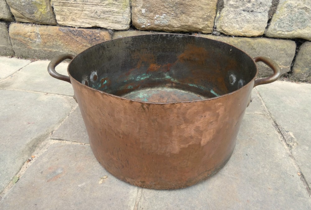 A large hand-hammered copper log bin featuring a wide cylindrical body, riveted side handles, and a natural aged patina with interior verdigris.