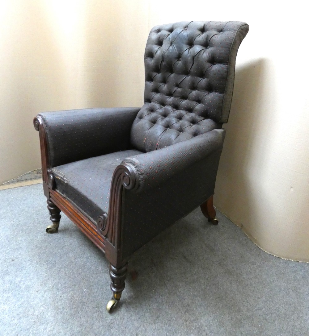 A William IV reclining library armchair featuring dark button-backed upholstery, mahogany scroll-carved arms, and turned legs with brass castors.