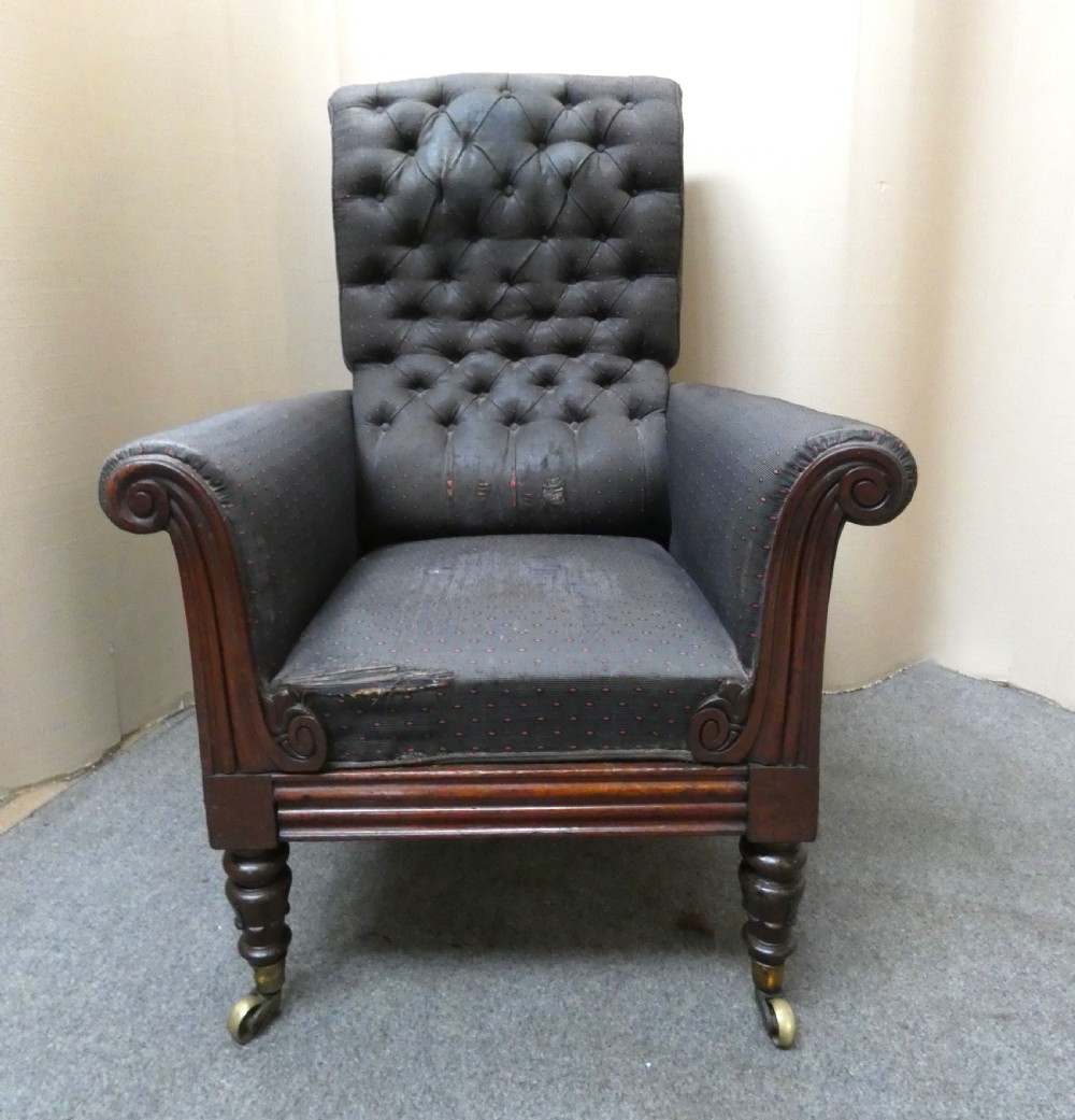 A William IV reclining library armchair featuring dark button-backed upholstery, mahogany scroll-carved arms, and turned legs with brass castors. View II