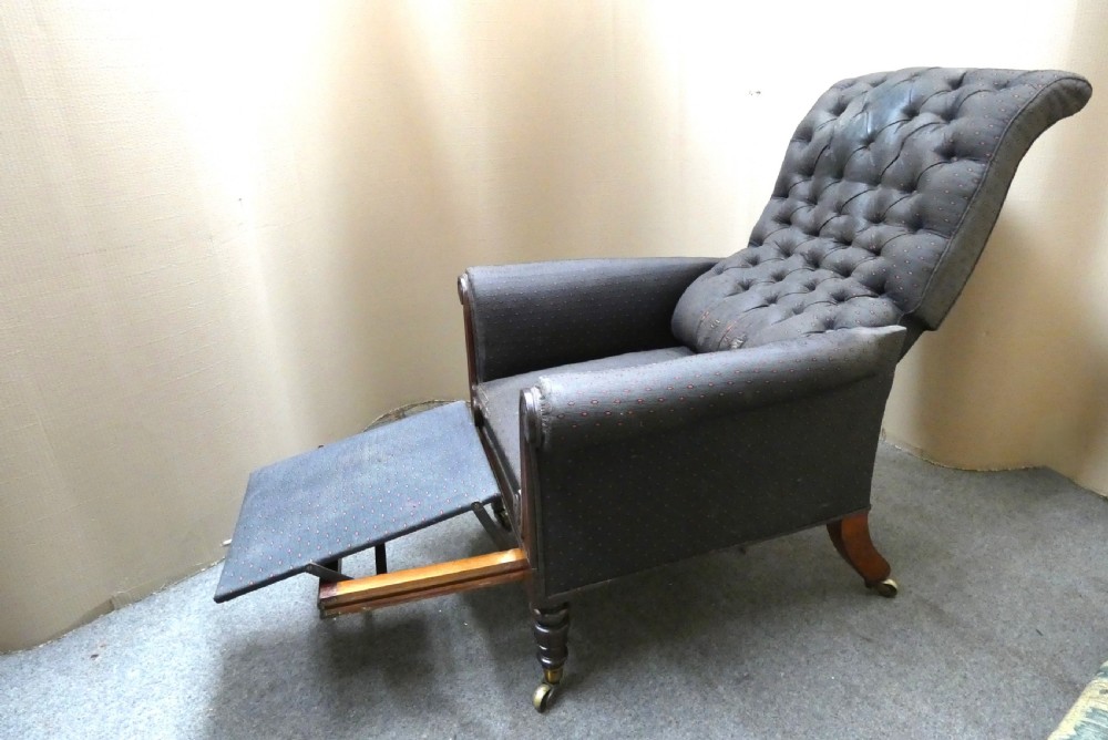 A William IV reclining library armchair featuring dark button-backed upholstery, mahogany scroll-carved arms, and turned legs with brass castors. View VI