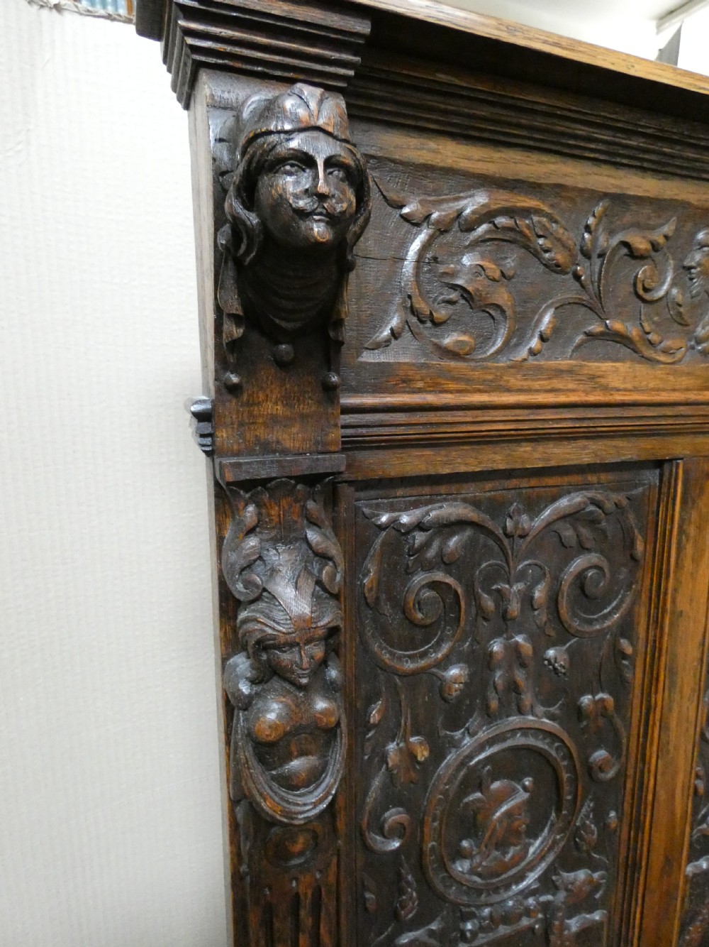 A dark carved oak high-back settle featuring three relief-carved back panels with portrait medallions, side caryatid figures, and a hinged storage seat above carved base panels. View V