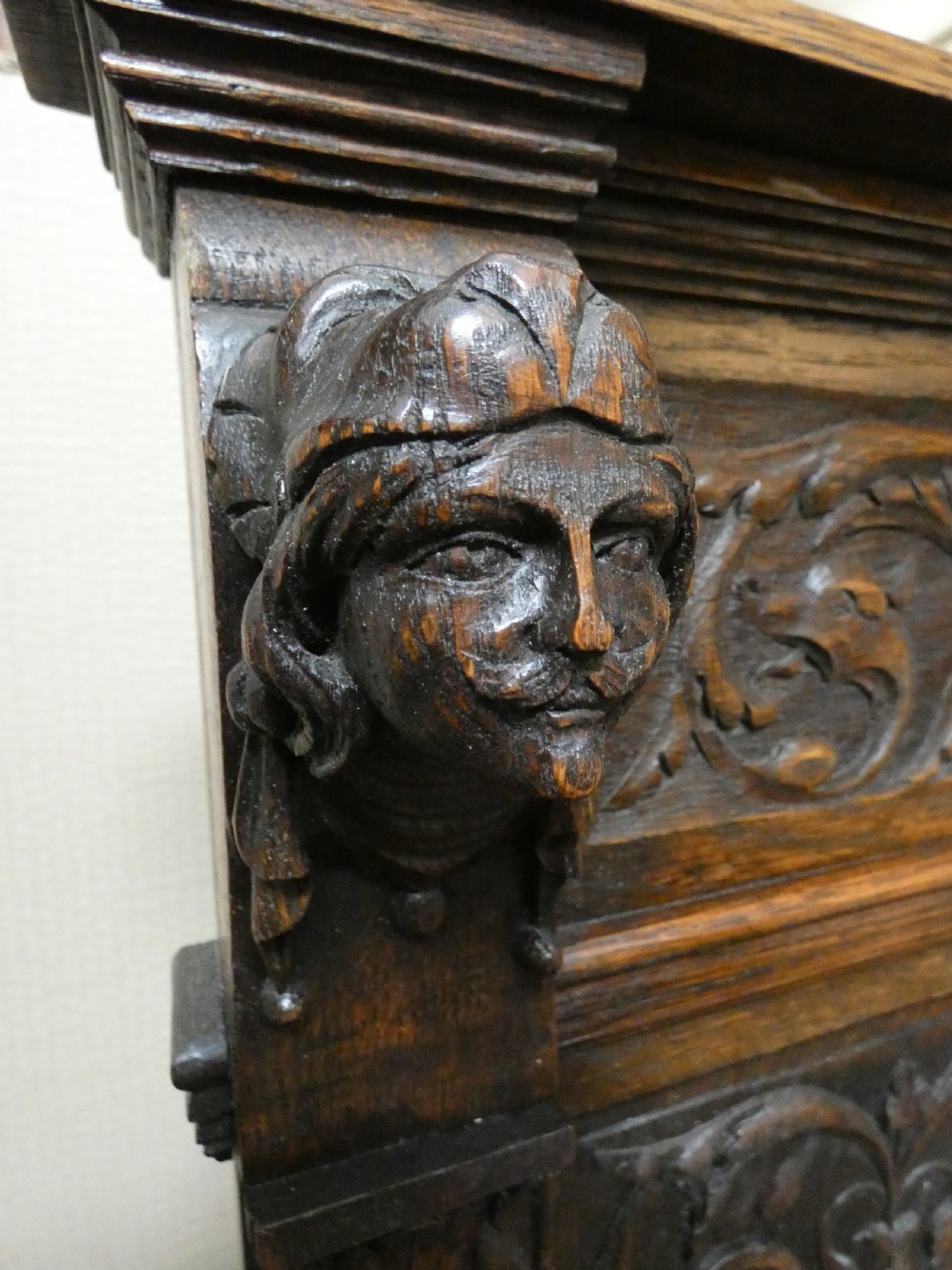 A dark carved oak high-back settle featuring three relief-carved back panels with portrait medallions, side caryatid figures, and a hinged storage seat above carved base panels. View VI