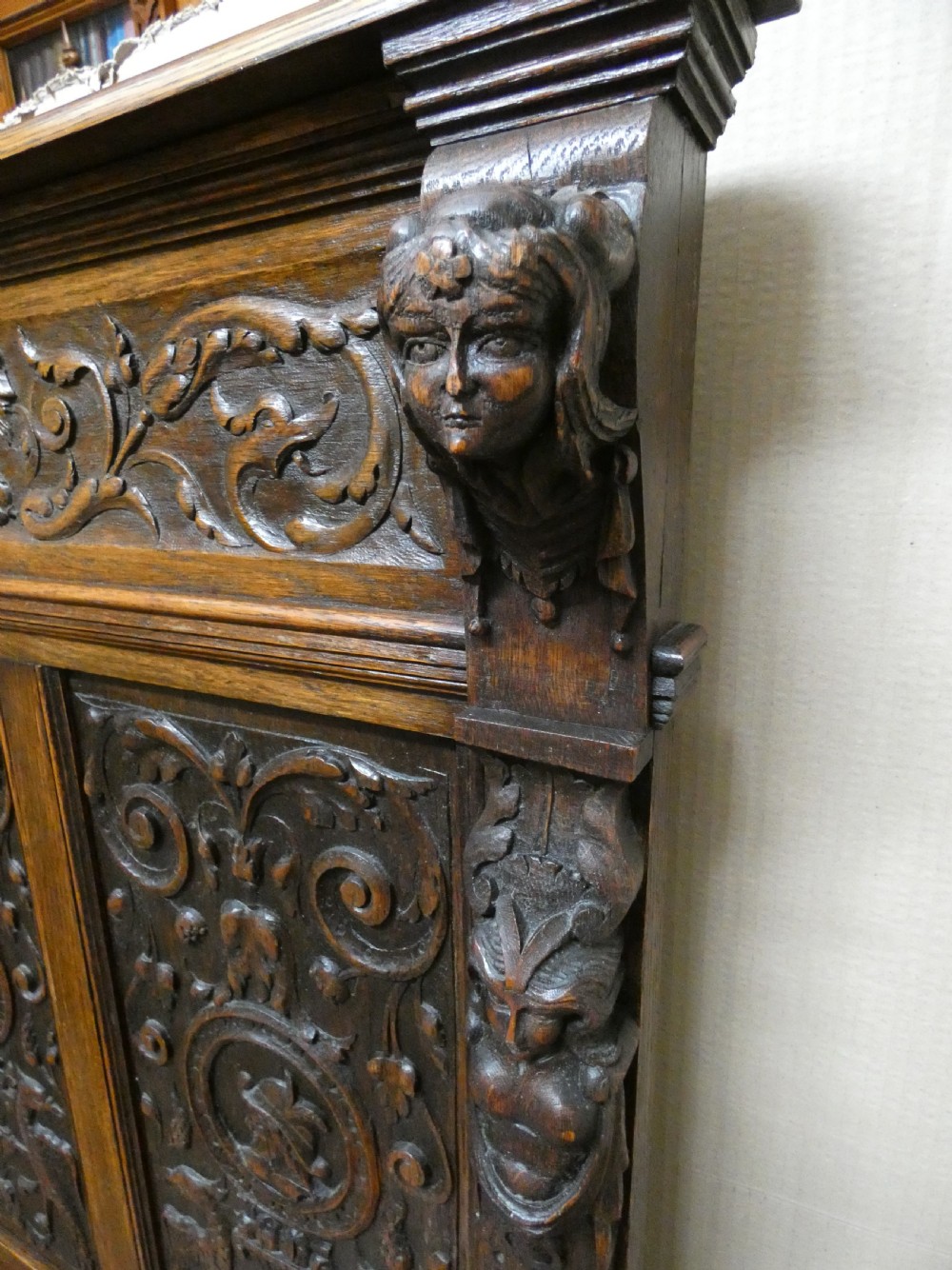 A dark carved oak high-back settle featuring three relief-carved back panels with portrait medallions, side caryatid figures, and a hinged storage seat above carved base panels. View IX