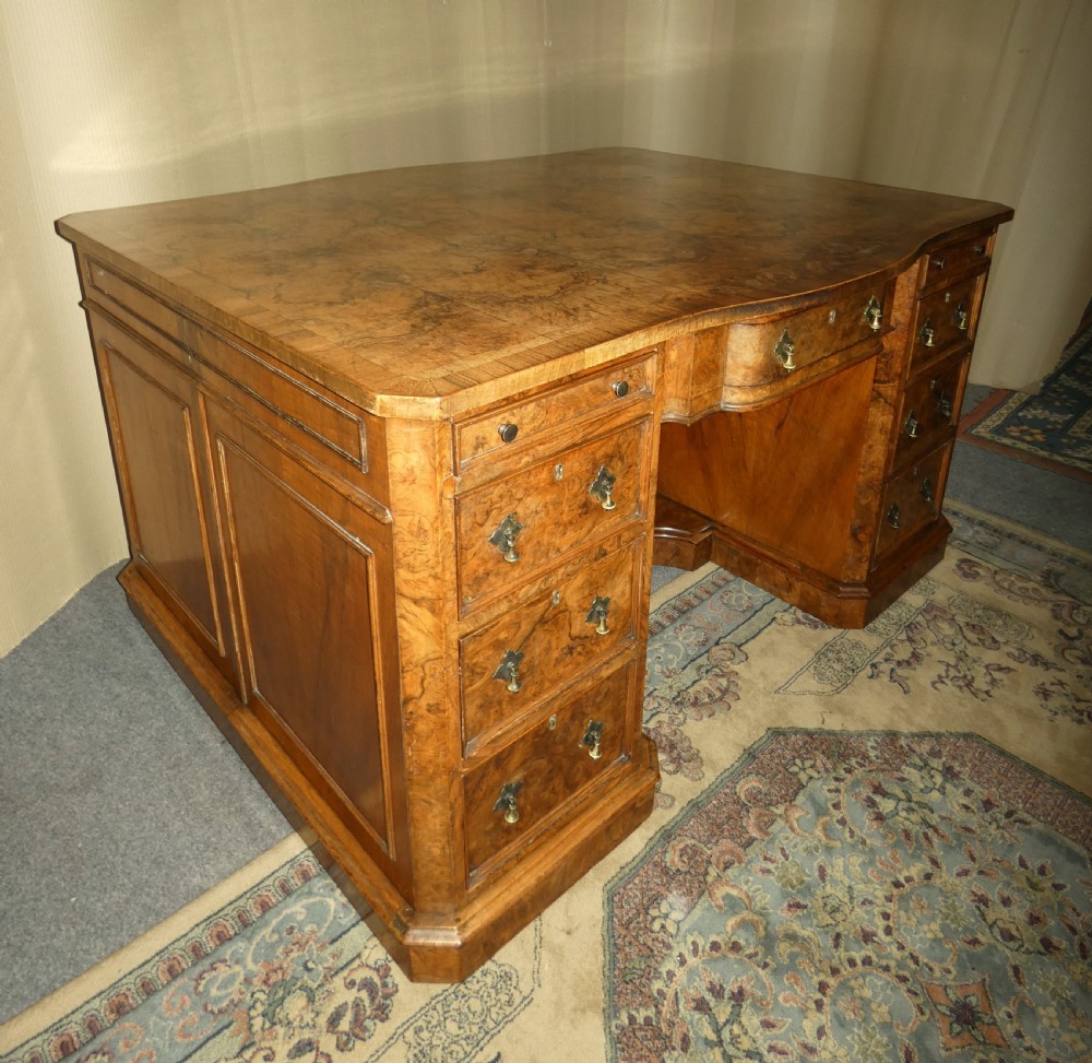 A large burr walnut partners desk featuring twin pedestals, multiple drawers with brass drop handles, and a crossbanded top surface.