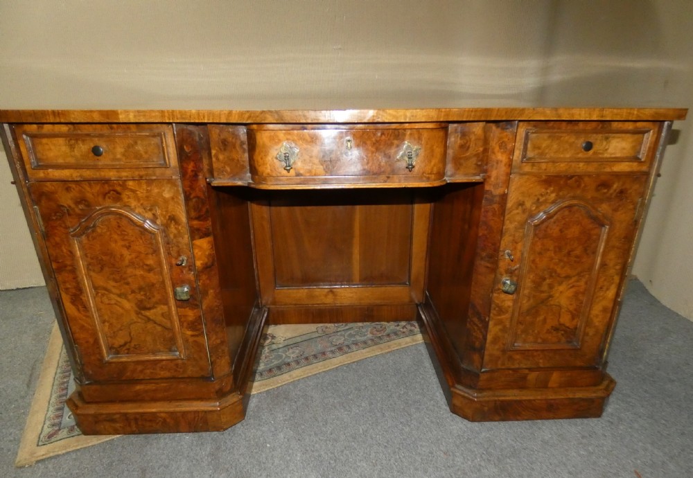A large burr walnut partners desk featuring twin pedestals, multiple drawers with brass drop handles, and a crossbanded top surface. View VII