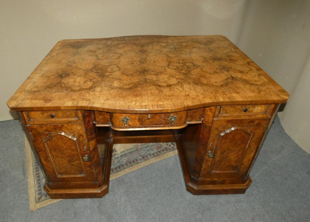 A large burr walnut partners desk featuring twin pedestals, multiple drawers with brass drop handles, and a crossbanded top surface. View IX