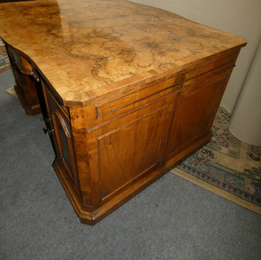 A large burr walnut partners desk featuring twin pedestals, multiple drawers with brass drop handles, and a crossbanded top surface. View X