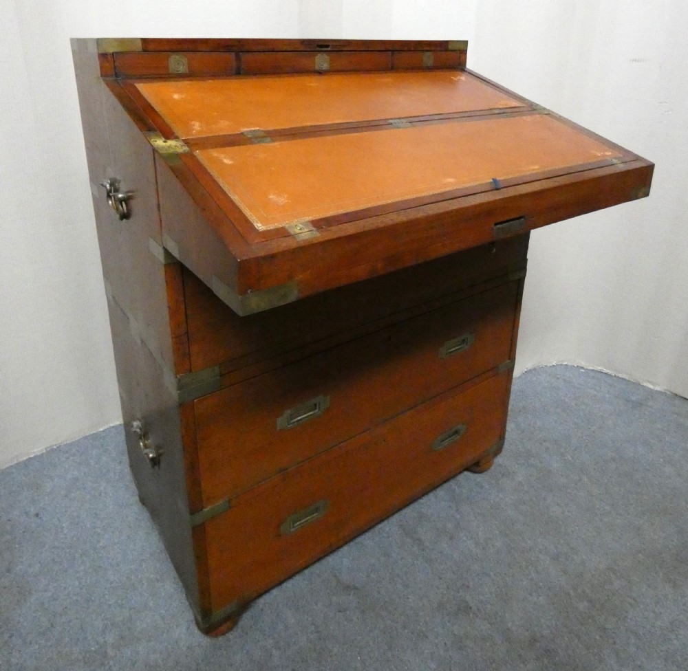 An antique teak campaign secretaire chest featuring brass corner mounts, flush drawer handles, carrying handles, and a drop-front slanted leather writing desk. View II