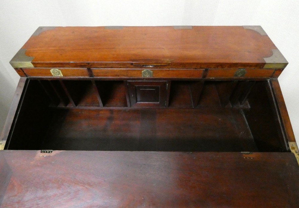 An antique teak campaign secretaire chest featuring brass corner mounts, flush drawer handles, carrying handles, and a drop-front slanted leather writing desk. View III