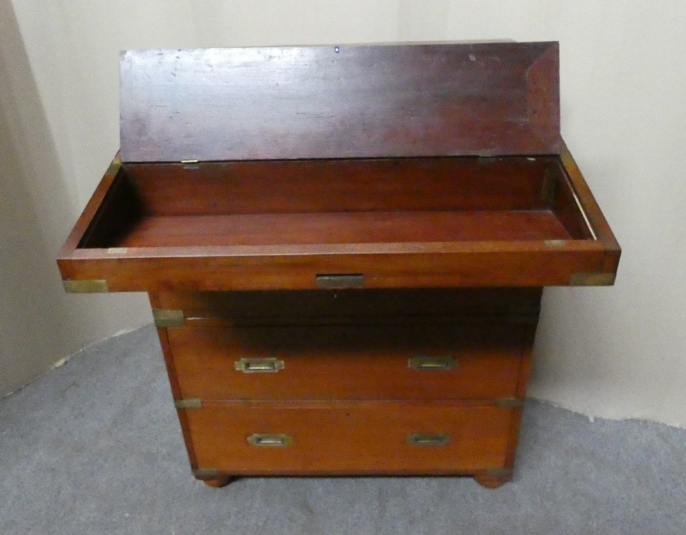 An antique teak campaign secretaire chest featuring brass corner mounts, flush drawer handles, carrying handles, and a drop-front slanted leather writing desk. View VI